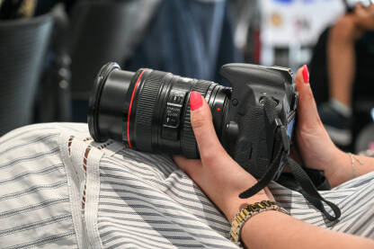 Djevojka drži profesionalni aparat u rukama. Djevojka drži profesionalni aparat u rukama. Profesionalna fotografkinja na događaju. Novinarka sa fotoaparatom. Mediji.