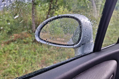 Kišne kapi na prozoru i retrovizoru automobila. Vožnja auta po kiši.