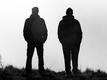 Dva planinara siluete Siluete dvojice planinara koji stoje na vrhu brda okrenuti prema kotlini ispunjenoj maglom
