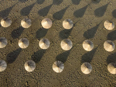 Suncobrani na praznoj pješčanoj plaži uz more, snimak dronom. Suncobrani na pješčanoj plaži uz more, snimak dronom. Suncobrani od trstike na obali mora.