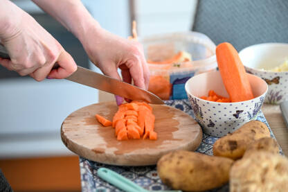 Djevojka nožem reže mrkvu na stolu. Sjeckanje povrće za ručak.