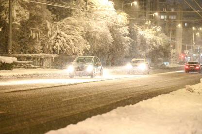 Automobili se kreću po snijegom pokrivenoj cesti. Vožnja vozila zimi dok pada snijeg. Pahuljice snijega padaju na cestu. Otežani i opasni uslovi vožnje.