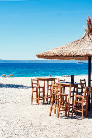 More Šljunčana plaža sa suncobranima od trske, ležaljkama, drvenim stolovima i stolicama i pogledom na ostrva Brač i Hvar. Makarska.