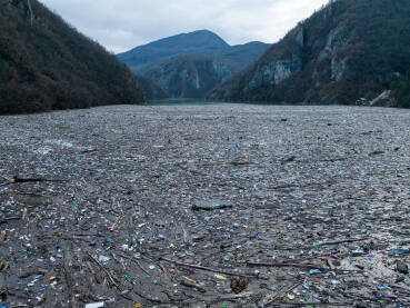 Razni oblici komunalnog otpada nagomilani u rijeci Drini, vidljivi na površini i uz obalu.