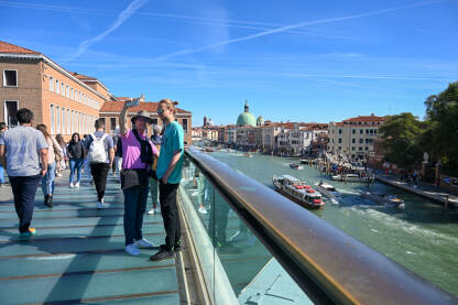 Venecija, Italija. Turisti fotografišu. Historijske zgrade duž riječnog kanala. Čamci i gondole na rijeci. Popularna turistička destinacija.
