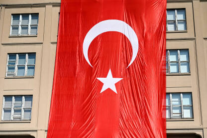 Turska zastava na zgradi. Ogromna turska zastava na zgradi. Nacionalna zastava Turske. Državni i nacionalni simbol. Crvena zastava s bijelom zvijezdom i polumjesecom. Turska.