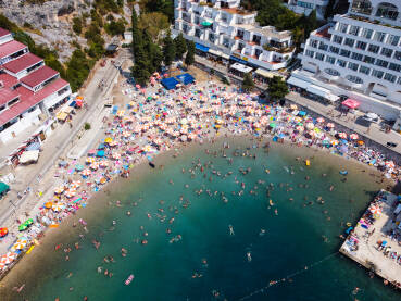 Mnogo turista u moru i na plaži na vrhuncu ljetne turističke sezone. Gomila ljudi koji se kupaju u moru. Ljudi u kupaćim kostimima na plaži, snimak dronom. Neum, BiH.