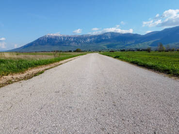 Duga ravna cesta u polju sa planinama u pozadini. Livanjsko polje i planina Kamešnica.