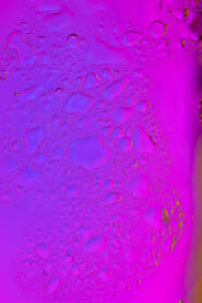 Kapljice vode na staklu Kapljice vode na staklu osvijetljenom u gradaciji neon pink / roze i ljubičaste boje.