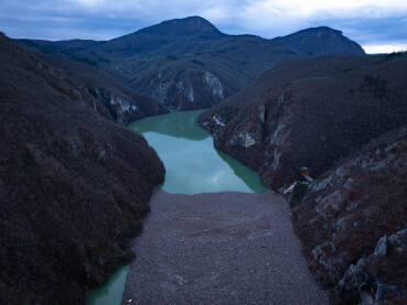 Razni oblici komunalnog otpada nagomilani u rijeci Drini, vidljivi na površini i uz obalu.