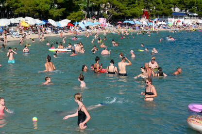 Plaža u Makarskoj puna ljudi Turisti na moru. Ljudi se kupaju i sunčaju u Jadranskom moru. Ljetni odmor. Grupa turista na plaži tokom toplog ljetnog dana. Makarska, Hrvatska.