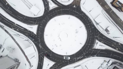 Snimak dronom na kružni tok u gradu tokom snježnih padavina. Automobili i kamioni se kreću u kružnom toku zimi. Snimak dronom na kružni tok u gradu tokom snježnih padavina.