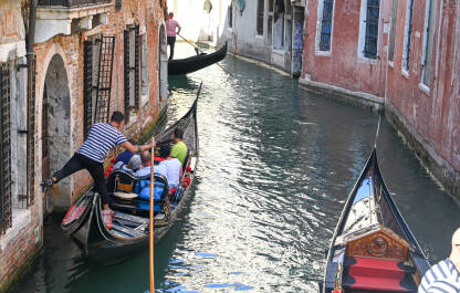 Venecija, Italija: Grupa turista uživa u vožnji gondolom. Venecija, Italija: Grupa turista uživa u vožnji gondolom kroz riječni kanal u centru grada. Popularno turističko odredište. Ljudi sjede u gondoli s gondolijerom.