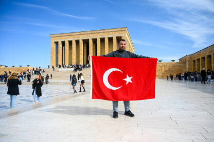 Muškarac drži zastavu Republike Turske ispred Anitkabira. Muškarac drži zastavu Republike Turske. Ljudi ispred mauzoleja Anitkabir. Anıtkabir je počivalište Mustafe Kemala Ataturka.