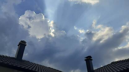 Sunce se probija kroz oblake iznad dimnjaka krova kuće.