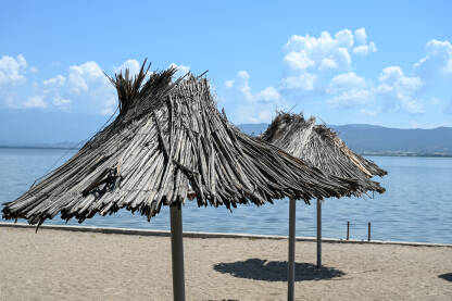 Suncobrani na praznoj plaži. Pusta plaža bez turista. Suncobrani na plaži. Dojransko jezero, Sjeverna Makedonija. Pješčana plaža pored jezera.