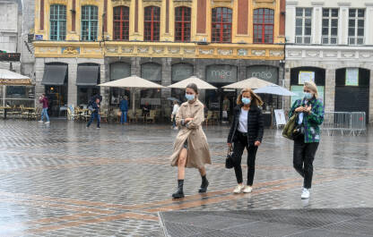 Djevojke hodaju po kiši. Žene sa maskama na licu šetaju ulicom. Pandemija korona virusa.