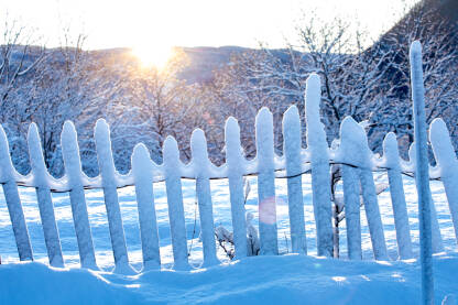 Drvena seoska ograda (taraba) prekrivena snijegom i jutarnje toplo sunce.