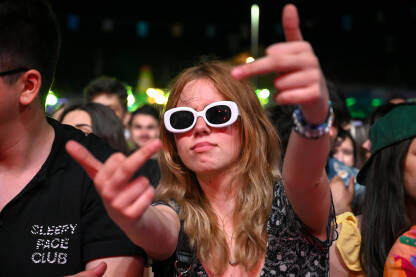 Publika na muzičkom festivalu Djevojka se zabavlja na muzičkom festivalu. Mlada djevojka nosi naočale i pokazuje srednji prst na koncertu.