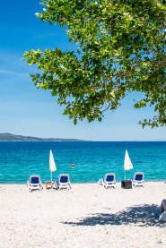 Plaža Šljunčana plaža sa suncobranima, ležaljkama i pogledom na ostrva Hvar i Brač. Makarska.