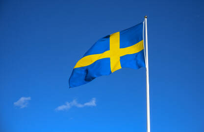 Švedska zastava na jarbolu naspram plavog neba. Zastava Švedske vijori se na jarbolu u Stockholmu. Švedska nacionalna zastava.