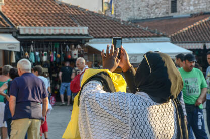 Žena pravi fotografiše mobilnim aparatom. Žena pravi fotografiše mobilnim aparatom. Turisti fotografišu ulice i zgrade.