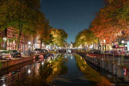 Amsterdam, Nizozemska. Kanal u centru grada. Amsterdam, Nizozemska. Zgrade, drveće, ulica i kanal u Amsterdamu noću. Grad navečer. Tipične i tradicionalne holandske kuće.