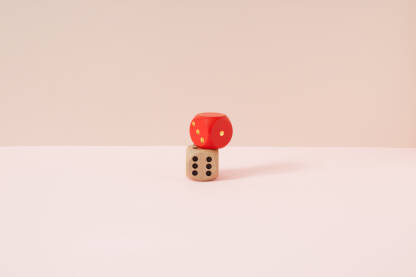 Kocke za igru u crvenoj i prirodnoj boji drveta s crnim točkama na bež i roze pozadini.