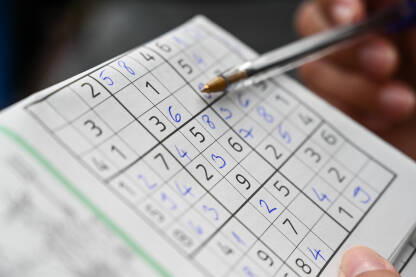 Mlada žena rješava sudoku zagonetku. Krupni plan žene koja drži olovku i rješava sudoku zagonetku. Osoba koja igra sudoku zagonetku. Djevojka igra sudoku.