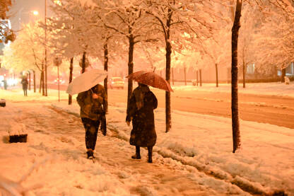 Ljudi hodaju s kišobranom kroz grad tokom zimskih sniježnih padavina. Pješaci u gradskoj ulici dok pada snijeg.