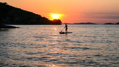 Djevojka vesla na dasci Djevojka vesla na dasci na moru. Žena uživa na Paddle-boardu ljeti. Veslanje na mirnom moru na zalasku sunca.