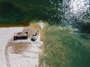 DJI_0078 Bager kopa i utovaruje pijesak u kamion na obali rijeke. Teški strojevi rade u kamenolomu pijeska. Snimak dronom na bager i kamion koji utovaruju šljunak u prirodi. Zagađenje okoliša i vode