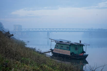 Zatvoreni savski čamac u maglovitom jutru sa mostom u pozadini