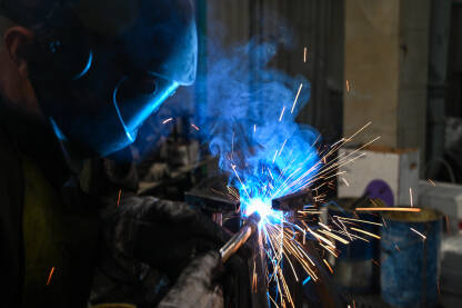 Zavarivač na poslu. Zavarivanje metala u fabrici. Varilac Zavarivač na poslu. Iskre. Radnik nosi kacigu i rukavice. Zavarivanje metala u fabrici. Krupni plan industrijskog radnika na gradilištu.
