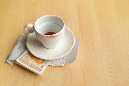 Šoljica popijenje kafe na stolu sa računom i novcem.