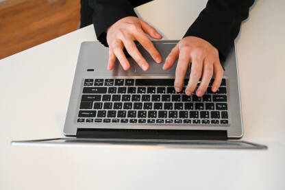 Osoba kuca na laptopu. Žena radi na laptopu, pogled odozgo. Ženske ruke kucaju na tastaturi. Djevojka koristi računar za stolom.