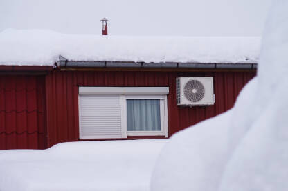 Grijanje na struju tokom zime. Snijeg na crvenom limenom krovu i klima uređaj.