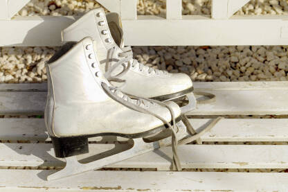 Stare bijele ženske klizaljke na klupi.