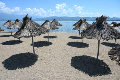 Suncobrani na praznoj plaži. Pusta plaža bez turista. Suncobrani na plaži. Dojransko jezero, Sjeverna Makedonija. Pješčana plaža pored jezera.