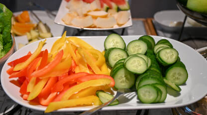 Tanjir sa narezanim crvenim i žutim paprikama i kolutovima krastavca. Svježa salata poslužena u restoranu.