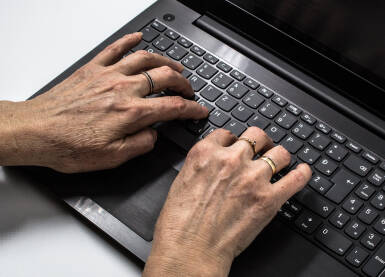 Stare ruke na tastaturi Starija ženska osoba kuca na tastaturi crnog lap-topa koji se nalazi na beloj pozadini. Stariji ljudi sve više uče da koriste računare.