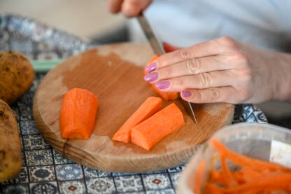 Djevojka nožem reže mrkvu na stolu. Sjeckanje povrće za ručak.