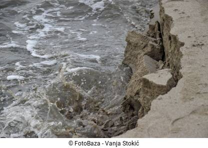 Erozija morske obale Poplava na moru. Bujica odnosi dio morske obale. Voda razara pješčanu obalu.