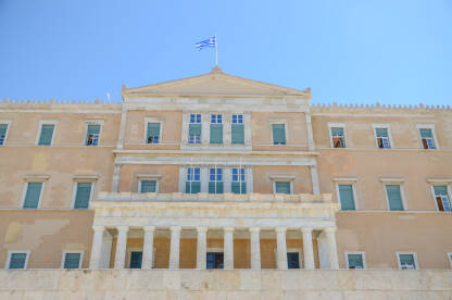 Atina, Grčka: Zgrada Helenskog parlamenta. Zastava Grčke. Stara kraljevska palata na trgu Sintagma, trenutno sjedište Grčkog parlamenta. Ljudi ispred institucije.
