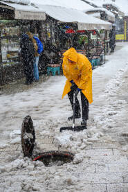 Radnik u žutom mantilu čisti plato Baščaršije i baca snijeg u otvoreni šaht tokom obilnih padavina.