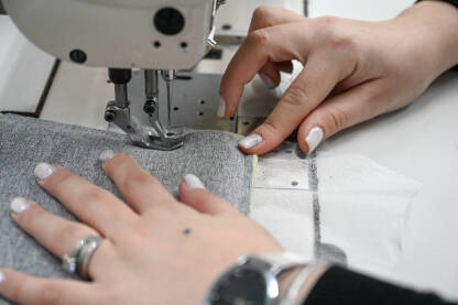 Žena šije tekstil šivaćom mašinom. Žena šije tekstil šivaćom mašinom. Radnica radi u fabrici.