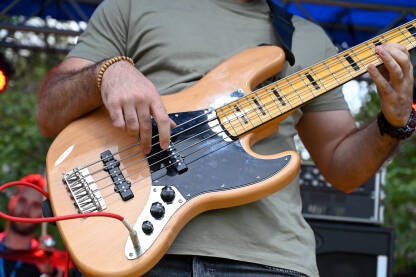 Muzičar svira električnu bas gitaru Muzičar svira električnu bas gitaru na bini. Čovjek svira bas gitaru s bendom na koncertu, krupni plan. Bas gitarista svira na festivalu. Muzički instrument
