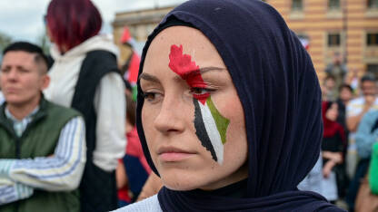 Žena sa palestinskom zastavom na licu na protestu. Žena sa palestinskom zastavom na licu. Protest podrške palestinskom narodu. Protest solidarnosti. Ljudi na demonstracijama u Sarajevu, BiH. Podrška narodu Gaze.
