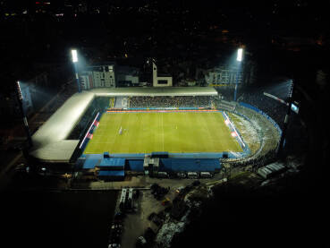 Fudbalski stadion Grbavica tokom fudbalske utakmice noću, snimak dronom. Fudbalski stadion tokom fudbalske utakmice noću, snimak dronom. Igrači na terenu. Zeleni sportski teren, svjetla i tribine na stadionu. Stadion Grbavica, Sarajevo.