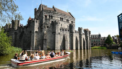 Gent, Belgija: Dvorac uz riječni kanal. Turisti na brodicama. Gent, Belgija: Dvorac uz riječni kanal u centru grada. Utvrđene kule i zidine na srednjovjekovnom utvrđenju. Turisti na brodicama.